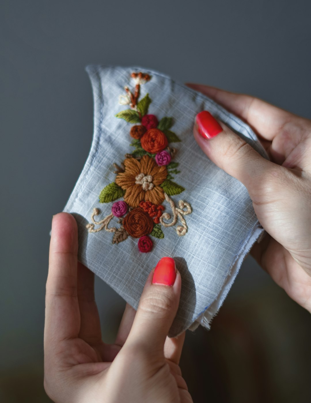 a-womans-hands-holding-a-piece-of-cloth-with-embroidered-flowers-on-it-5fj8pnlntg0